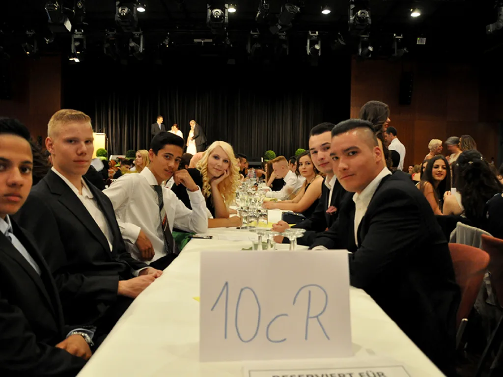 Jugendliche an einer Tafel mit dem Tischschild einer Klasse.